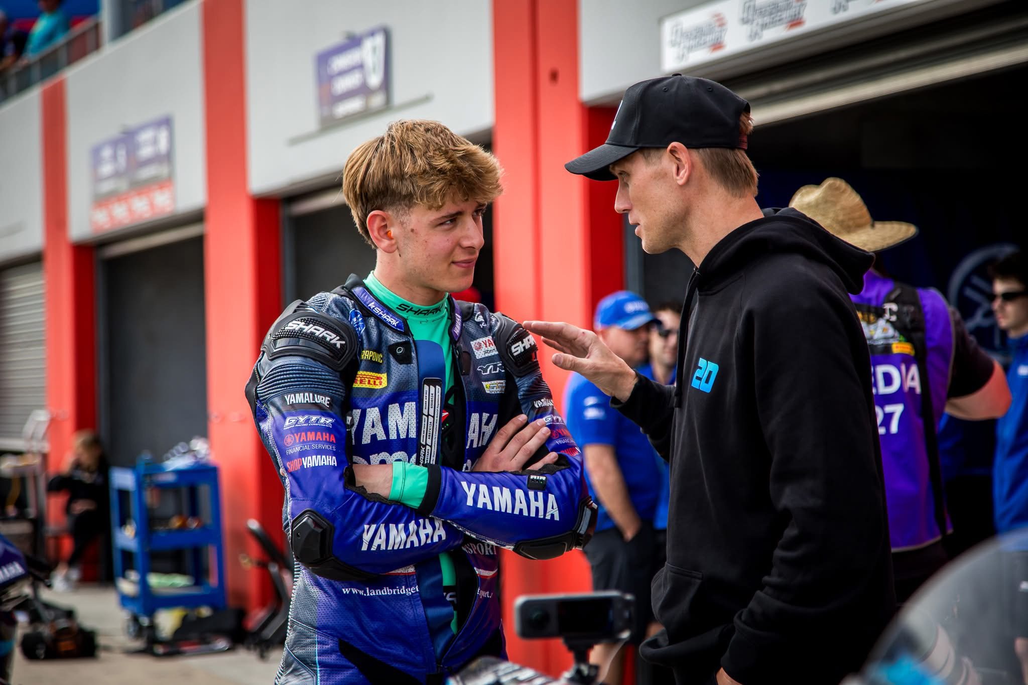 Troy Herfoss mentoring a young motorcycle racer in pit lane at a race meeting